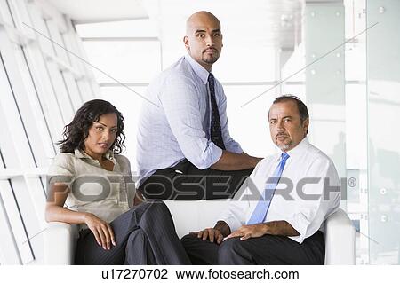 Stock Image - Three businesspeople sitting indoors (high key/selective focus). Fotosearch