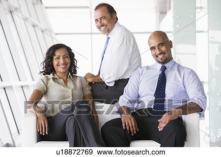 Stock Photo - Three businesspeople sitting indoors smiling (high key/selective focus). Fotosearch