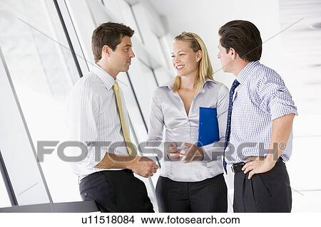 Three businesspeople standing in corridor talking and smiling View Large Photo Image Picture - Three businesspeople standing in corridor talking and smiling. Fotosearch