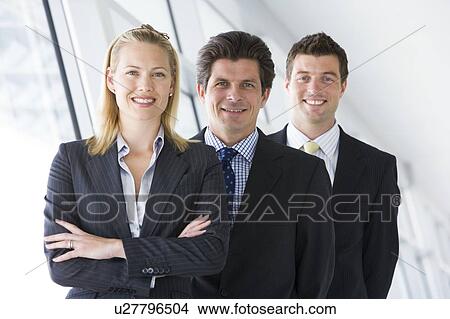 Picture - Three businesspeople standing in corridor smiling. Fotosearch