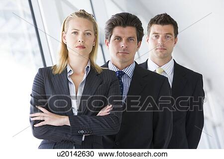 Stock Image - Three businesspeople standing in corridor. Fotosearch
