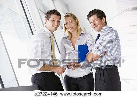 Three businesspeople standing in corridor smiling View Large Photo Image Stock Photograph - Three businesspeople standing in corridor smiling. Fotosearch