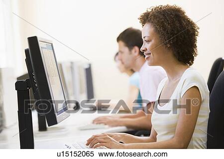 Stock Photography - Three people sitting in computer room typing and smiling. Fotosearch