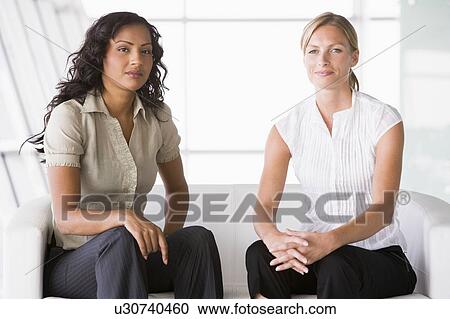 Two businesswomen sitting indoors smiling (high key/selective focus) View Large Photo Image Stock Image - Two businesswomen sitting indoors smiling (high key/selective focus). Fotosearch