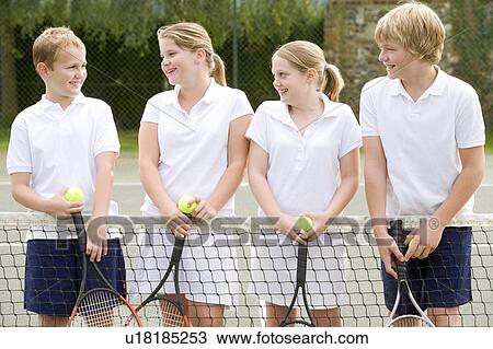 Stock Image - Four young friends with rackets on tennis court smiling. Fotosearch