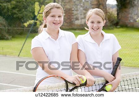 Stock Photography - Two young girl friends with rackets on tennis court smiling. Fotosearch