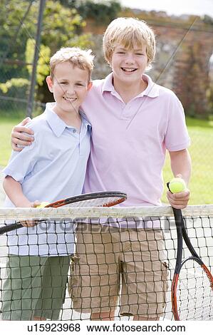 Stock Photo - Two young male friends with rackets on tennis court smiling. Fotosearch
