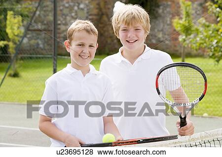 Two young male friends with rackets on tennis court smiling View Large Photo Image Stock Photo - Two young male friends with rackets on tennis court smiling. Fotosearch