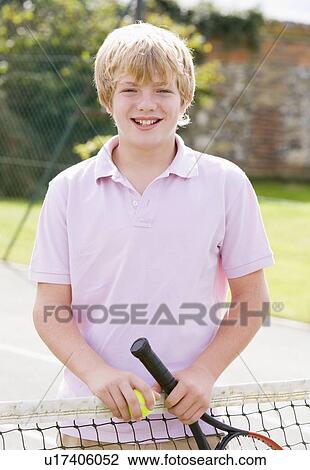 Stock Image - Young boy with racket on tennis court smiling. Fotosearch
