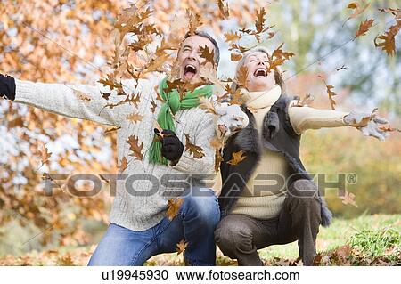 Stock Image - Couple outdoors playing in leaves and smiling (selective focus). Fotosearch