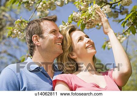 Stock Image - Couple standing outdoors holding blossom smiling. Fotosearch