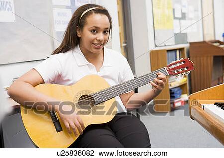 Stock Image - Female student learning guitar in classroom. Fotosearch