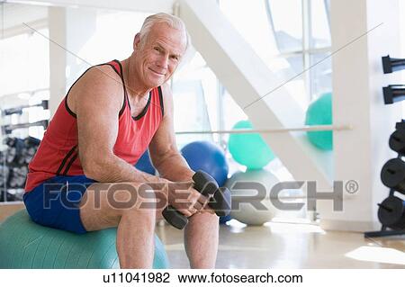 Stock Image - Man Using Hand Weights On Swiss Ball At Gym. Fotosearch