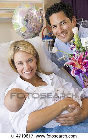 Stock Photo - New mother with baby and husband in hospital smiling. Fotosearch