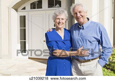 Stock Photo - Senior couple standing outside their home. Fotosearch