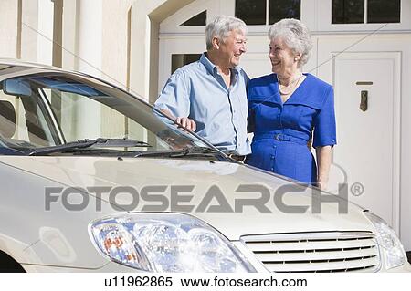 Stock Photography - Senior couple standing with their car outside their home. Fotosearch