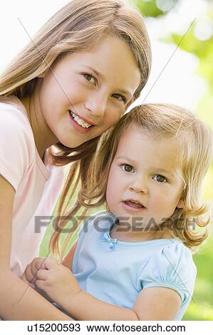 Stock Image - Two sisters sitting outdoors smiling. Fotosearch