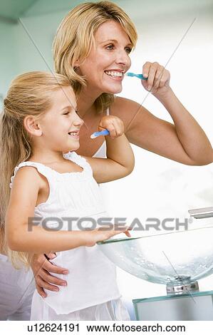 Stock Image - Woman and young girl in bathroom brushing teeth. Fotosearch