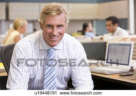 Stock Image - Businessman in cubicle smiling. Fotosearch
