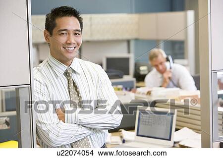 Picture - Businessman standing in cubicle smiling. Fotosearch