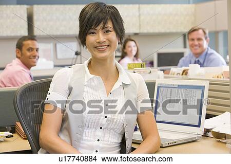 Picture - Businesswoman in cubicle smiling. Fotosearch