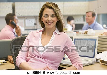 Stock Photograph - Businesswoman in cubicle smiling. Fotosearch