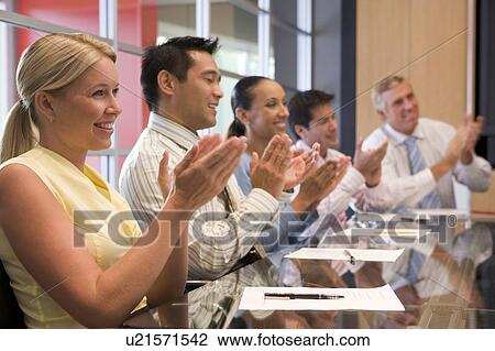 Stock Image - Five businesspeople at boardroom table applauding and smiling. Fotosearch