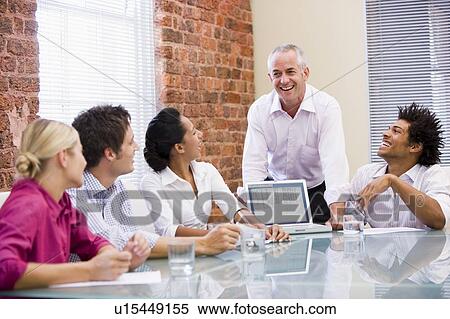 Stock Photography - Five businesspeople in boardroom with laptop laughing. Fotosearch