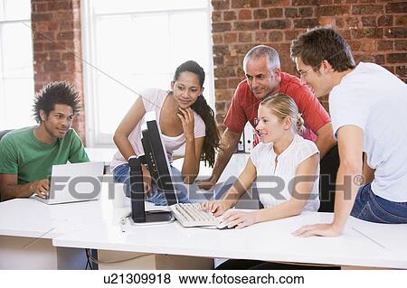 Stock Photo - Five businesspeople in office space looking at computer and smiling. Fotosearch