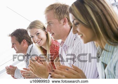 Stock Image - Four businesspeople applauding indoors smiling. Fotosearch