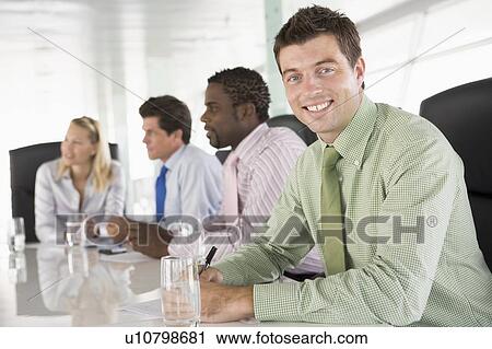 Stock Image - Four businesspeople in a boardroom smiling. Fotosearch