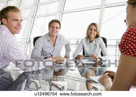 Picture - Four businesspeople in a boardroom with paperwork smiling. Fotosearch