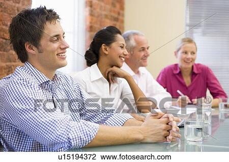 Stock Image - Four businesspeople in boardroom smiling. Fotosearch