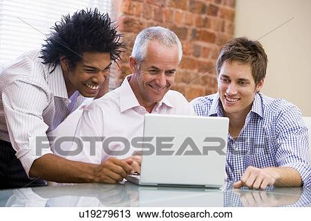 Three businessmen sitting in office with laptop smiling View Large Photo Image Stock Image - Three businessmen sitting in office with laptop smiling. Fotosearch