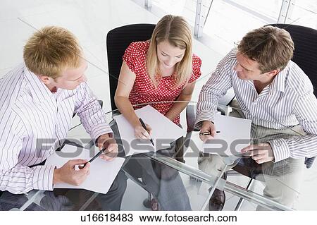 Stock Image - Three businesspeople in boardroom with paperwork. Fotosearch