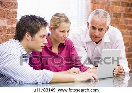 Stock Photo - Three businesspeople in office looking at laptop. Fotosearch