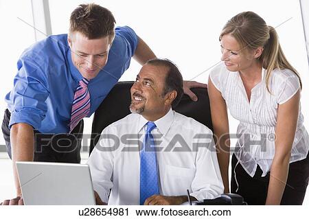 Stock Image - Three businesspeople in office with laptop talking and smiling (high key/selective focus). Fotosearch