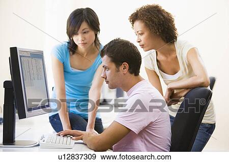 Three people sitting in computer room looking at monitor View Large Photo Image Stock Photo - Three people sitting in computer room looking at monitor. Fotosearch