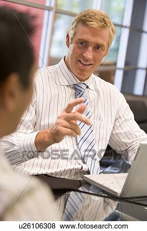 Two businessmen in boardroom with laptop talking View Large Photo Image Stock Photo - Two businessmen in boardroom with laptop talking. Fotosearch