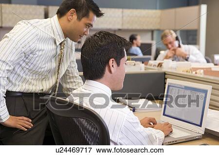 Two businessmen in cubicle looking at laptop View Large Photo Image Stock Photo - Two businessmen in cubicle looking at laptop. Fotosearch