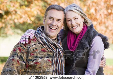 Stock Photo - Couple outdoors in park embracing and smiling (selective focus). Fotosearch