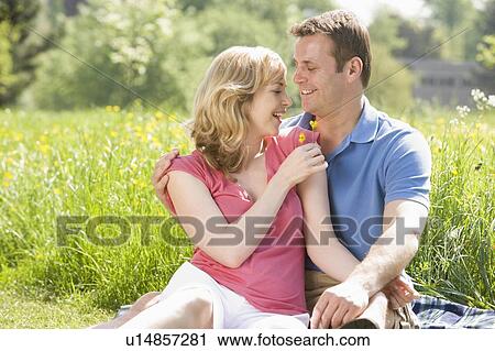 Stock Image - Couple sitting outdoors holding flower smiling. Fotosearch