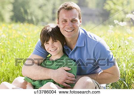 Picture - Father and son sitting outdoors smiling. Fotosearch