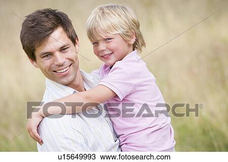 Stock Image - Father holding son outdoors smiling. Fotosearch