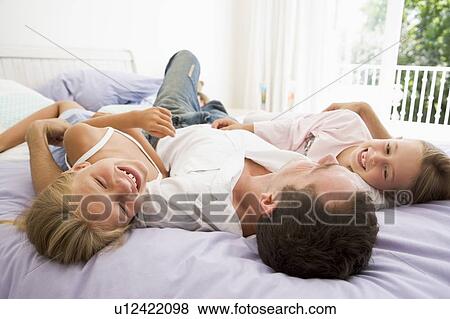 Man lying in bed with two young girls smiling View Large Photo Image Stock Photo - Man lying in bed with two young girls smiling. Fotosearch