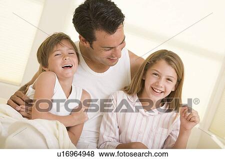 Man with two young children sitting in bed smiling View Large Photo Image Stock Photo - Man with two young children sitting in bed smiling. Fotosearch