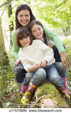 Mother and daughters outdoors in woods sitting on log smiling View Large Photo Image Stock Image - Mother and daughters outdoors in woods sitting on log smiling. Fotosearch