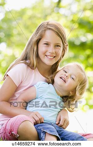 Two sisters sitting outdoors smiling View Large Photo Image Picture - Two sisters sitting outdoors smiling. Fotosearch
