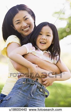 Stock Image - Woman and young girl outdoors embracing and smiling. Fotosearch