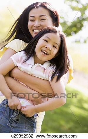 Stock Image - Woman and young girl outdoors embracing and smiling. Fotosearch